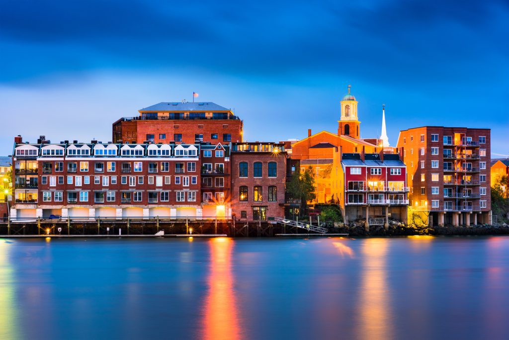 Portsmouth's harbor at night, brick. buildings lit up with light, the sky dark blue.