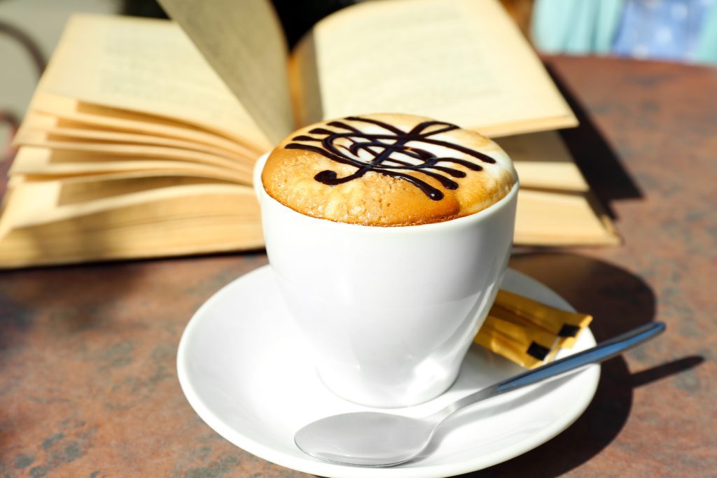 A cappuccino next to an open book.