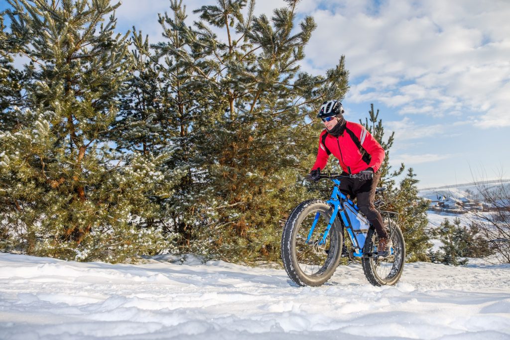 A man in a red jacket riding a fat tire bike through a snowy forest.