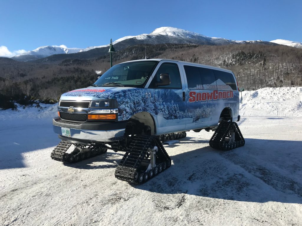 An SUV-like vehicle with four tracks instead of tires, Mount Washington in the background.