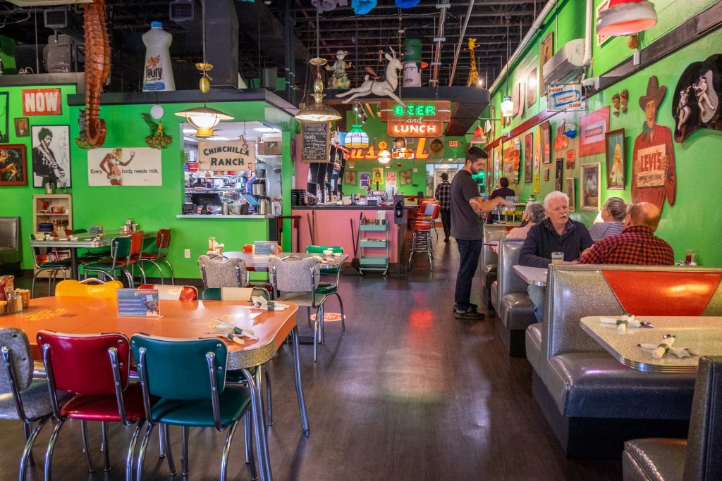A bright and colorful vintage diner with bright green walls and lots of neon signs and plastic and chrome furniture.