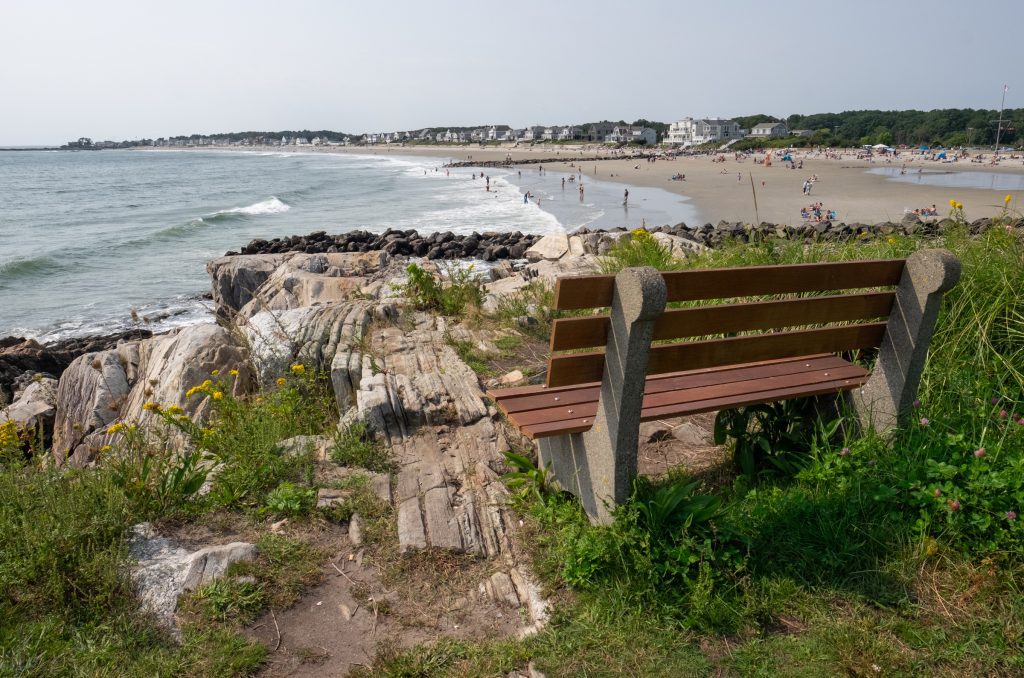 A wooden bench perched on a hill overlooking a long, wide beach.