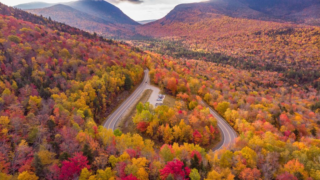 A highway curving through mountains covered with red, orange, and yellow trees.