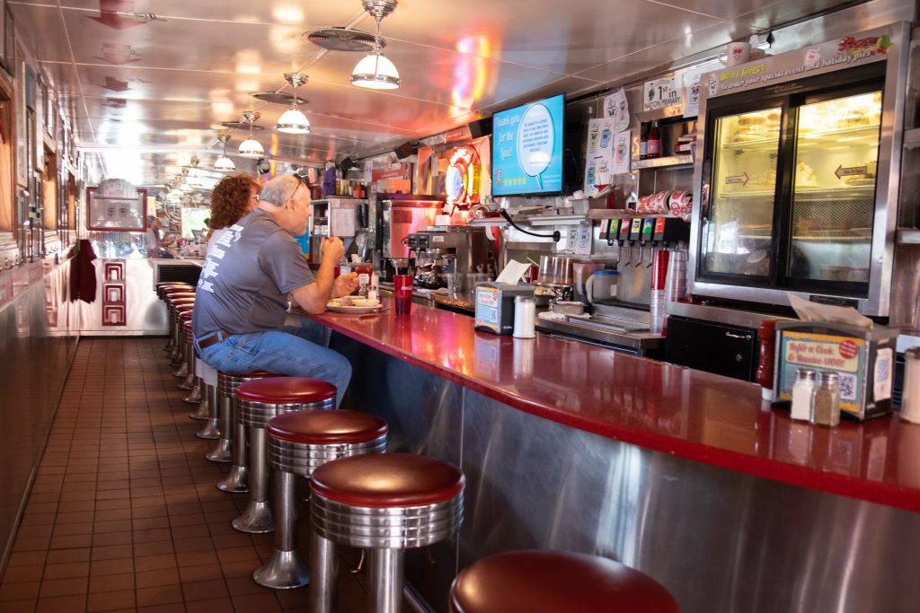 A narrow diner with red bar stools and a red countertop.
