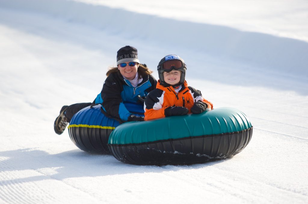 A mom and son snow tubing down a hill together.