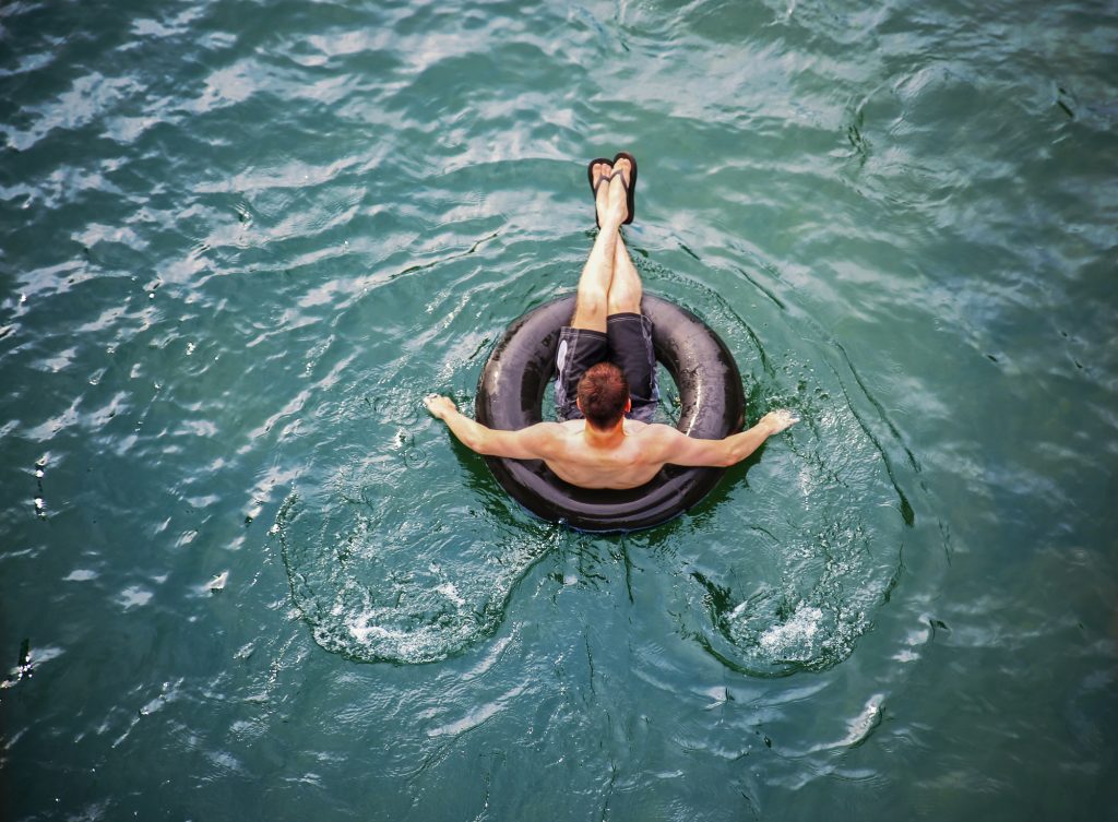 A man floating along alone in a black inner tube on a teal river.