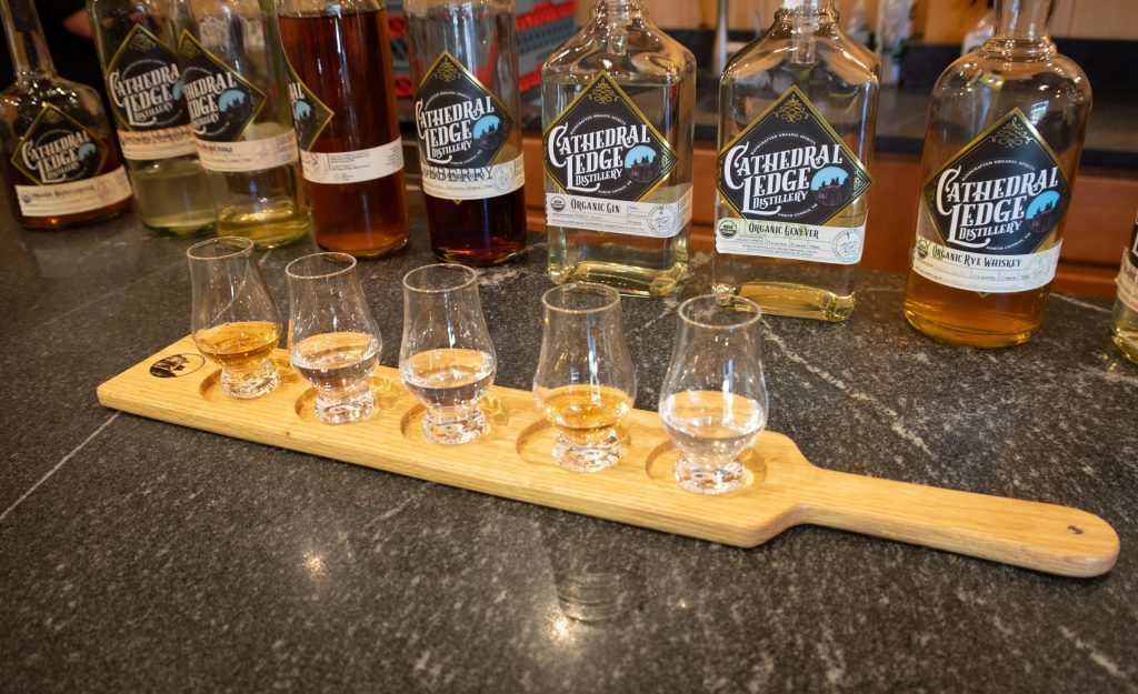A paddle of five shot glasses with spirits in front of Cathedral Ledge bottles of spirits.