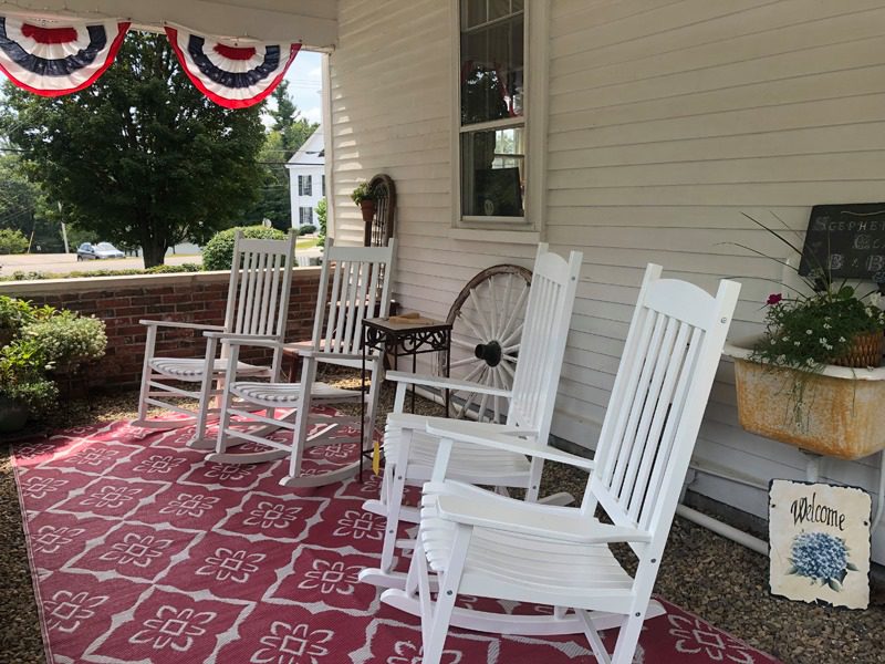 Four white rocking chairs on a front porch with a red carpet