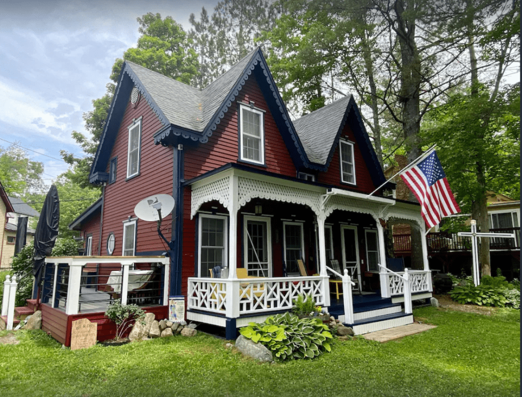 A red 4 bedroom cottage with green roof and white front porch, with an American flag hanging on the front