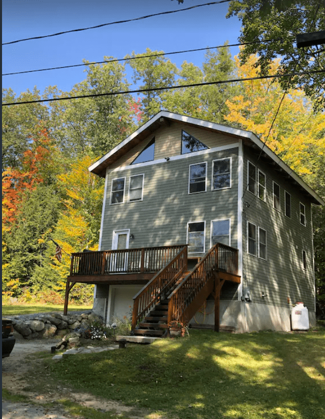 A view of a two story green Lake Sunapee cottage with a wooden deck