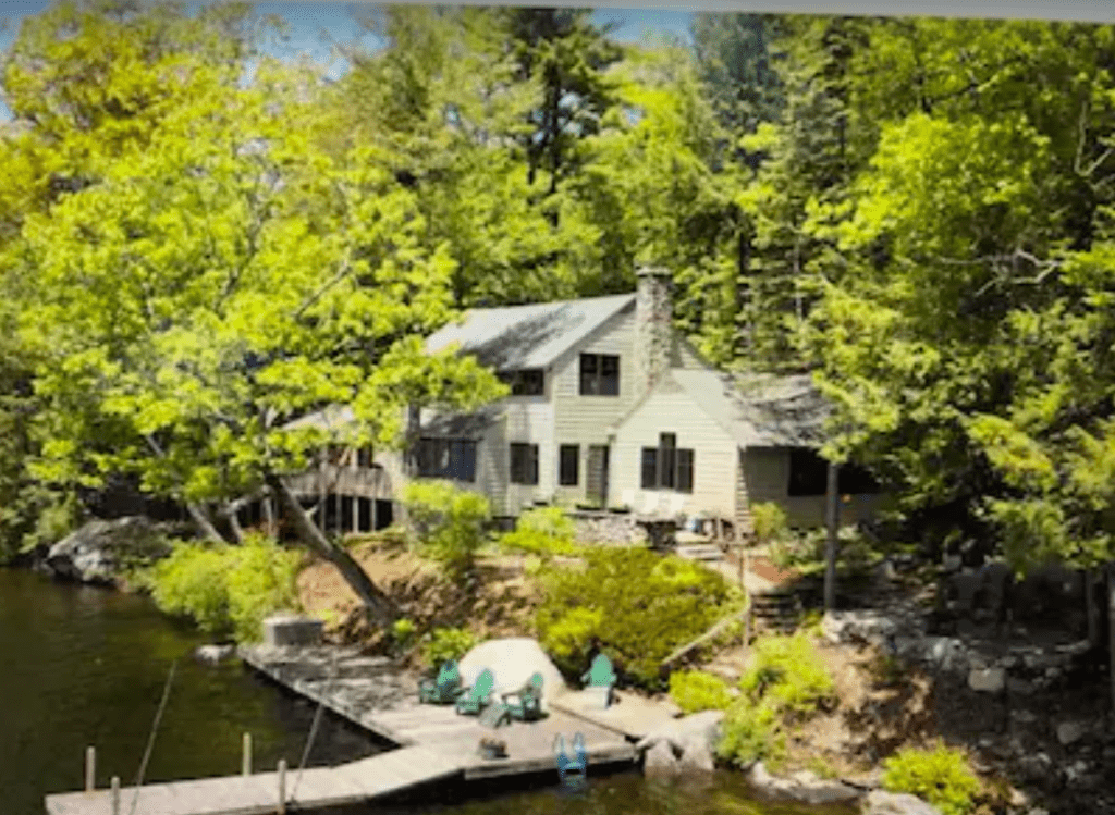 Aerial view of a large lake cottage tucked away behind spring foliage with a private dock onto Lake Sunapee