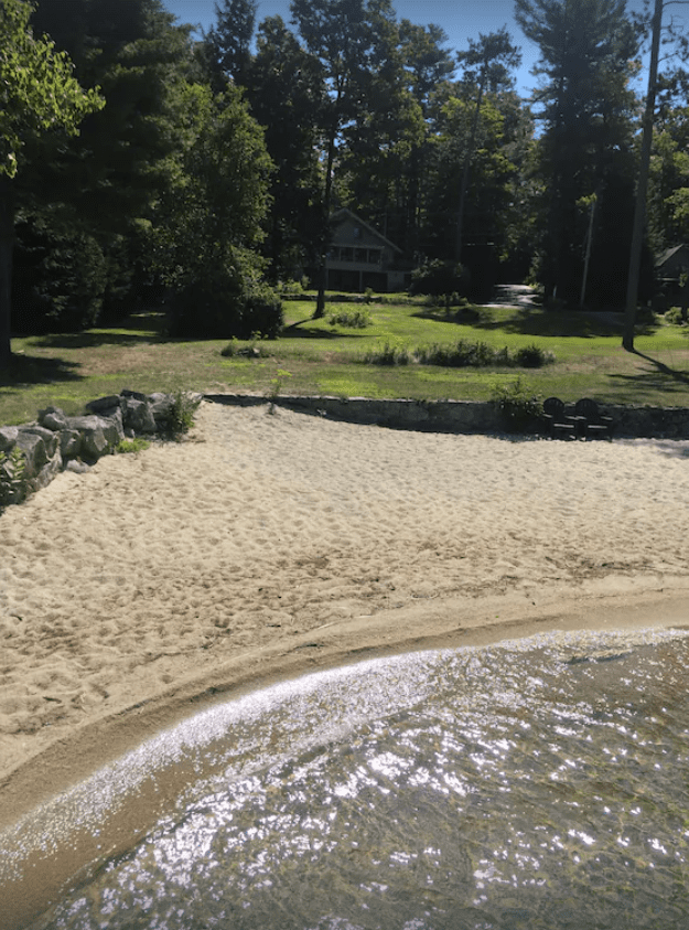 The edge of Lake Sunapee onto a sandy beach, with a house in the background