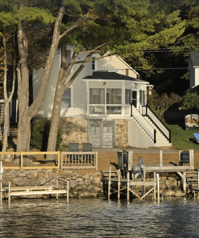 View of a gray lakehouse with a private dock from Lake Sunapee