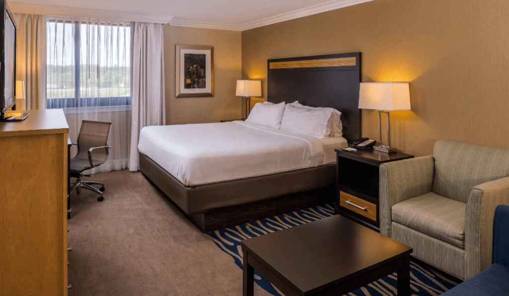 A basic hotel room with a queen bed and green chair