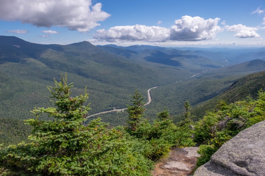 From above, a highway slinking between two mountain ranges covered with green trees.