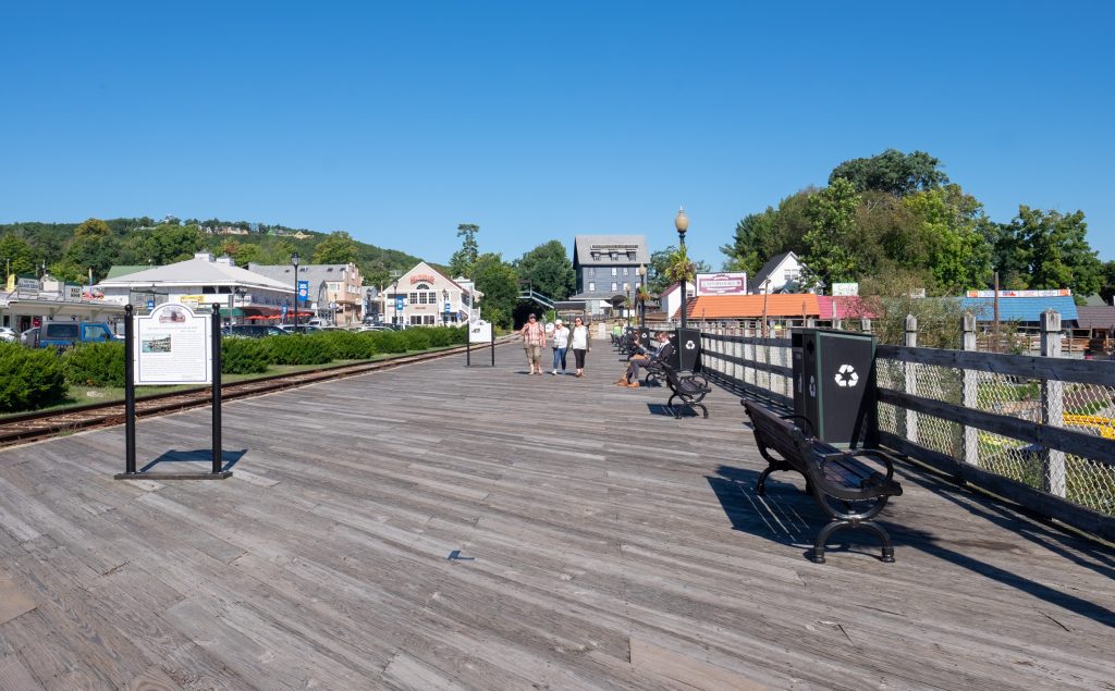 A wide wooden boardwalk lined with plaques with writing. Some benches to the side.