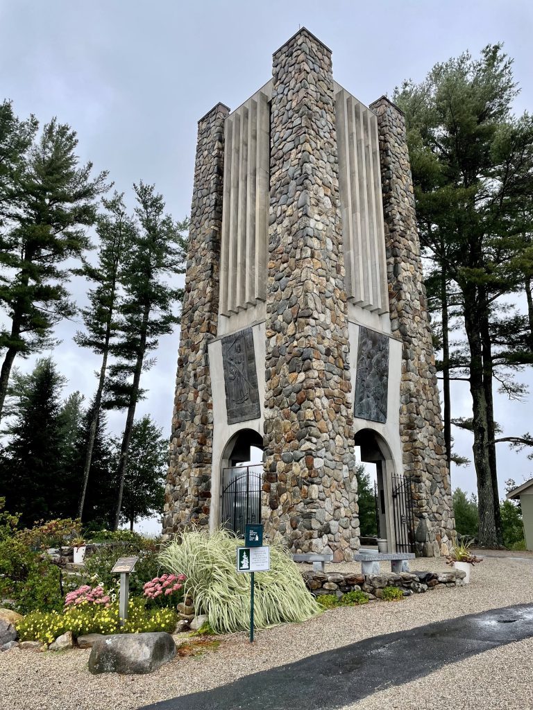 A tall stone rectangular chapel-like building surrounded by plants and trees.