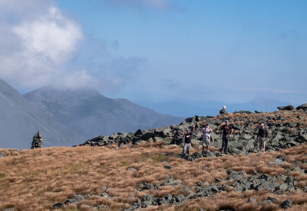Four men hiking on a rocky overlook and waving to the camera.
