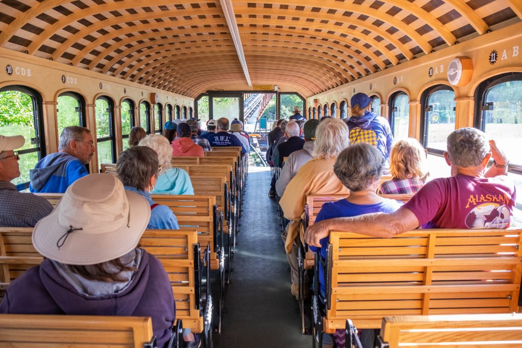 The inside of a train car, all wood with tows of two benches each sitting two people, an aisle down the middle.