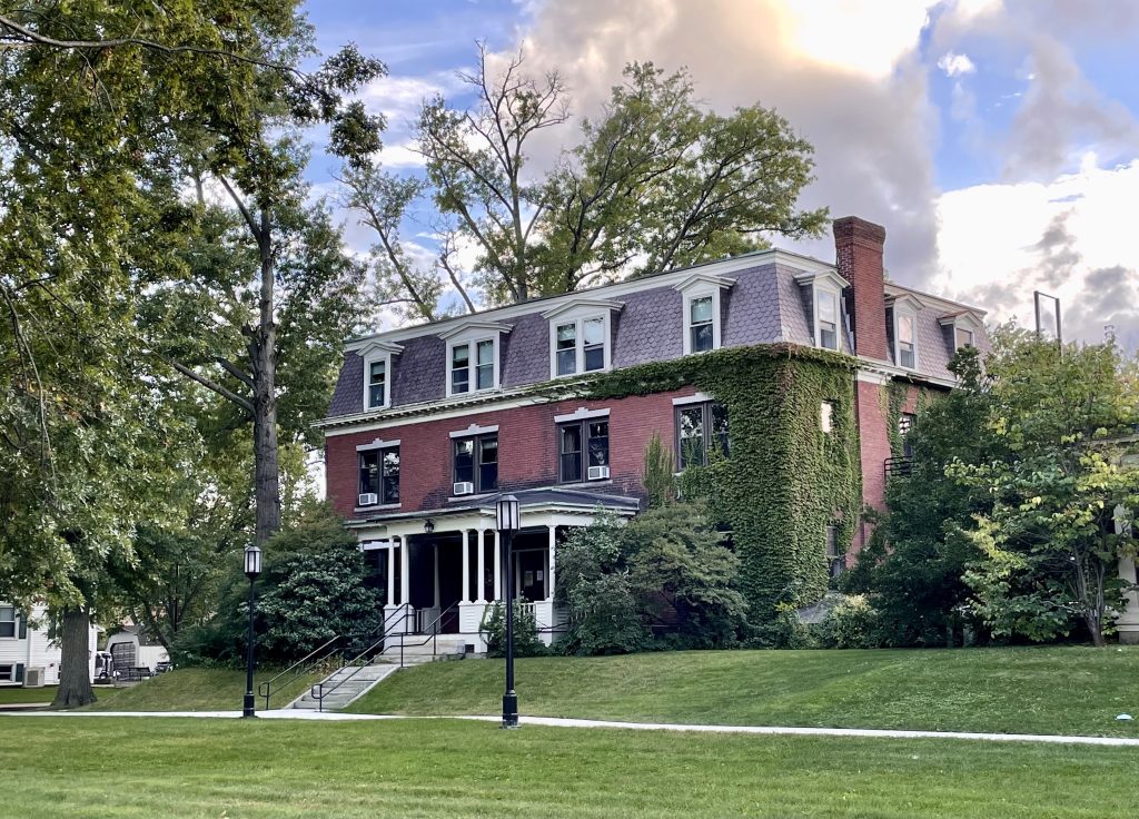 An elegant brick building covered in ivy with a porch with columns.