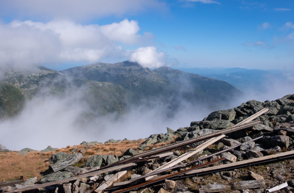 Views of mountains engulfed by clouds surrounded by blue sky.