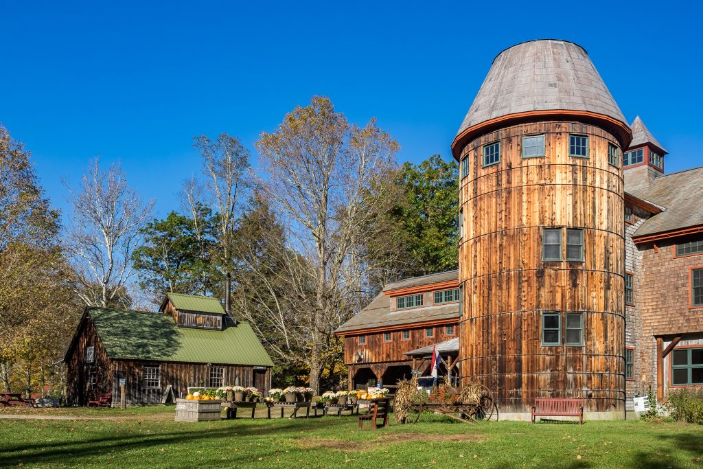 A farm building with a tall, wide round grain silo. On the ground are pots of flowers.