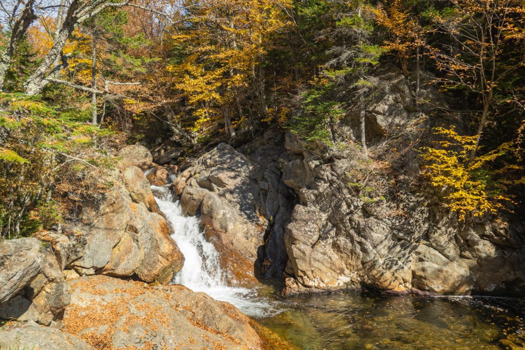 A small waterfall surrounded by granite walls leading into a river.
