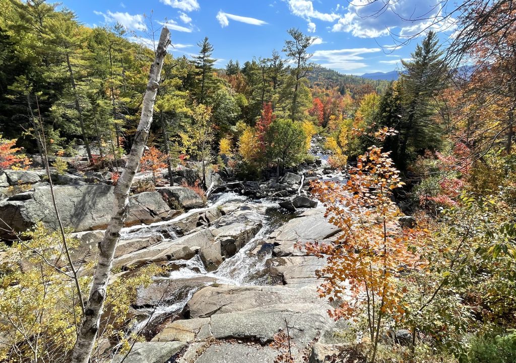 Looking downhill at countless waterfalls flowing over rocks, surrounded by fall foliage trees of red, orange, and green.