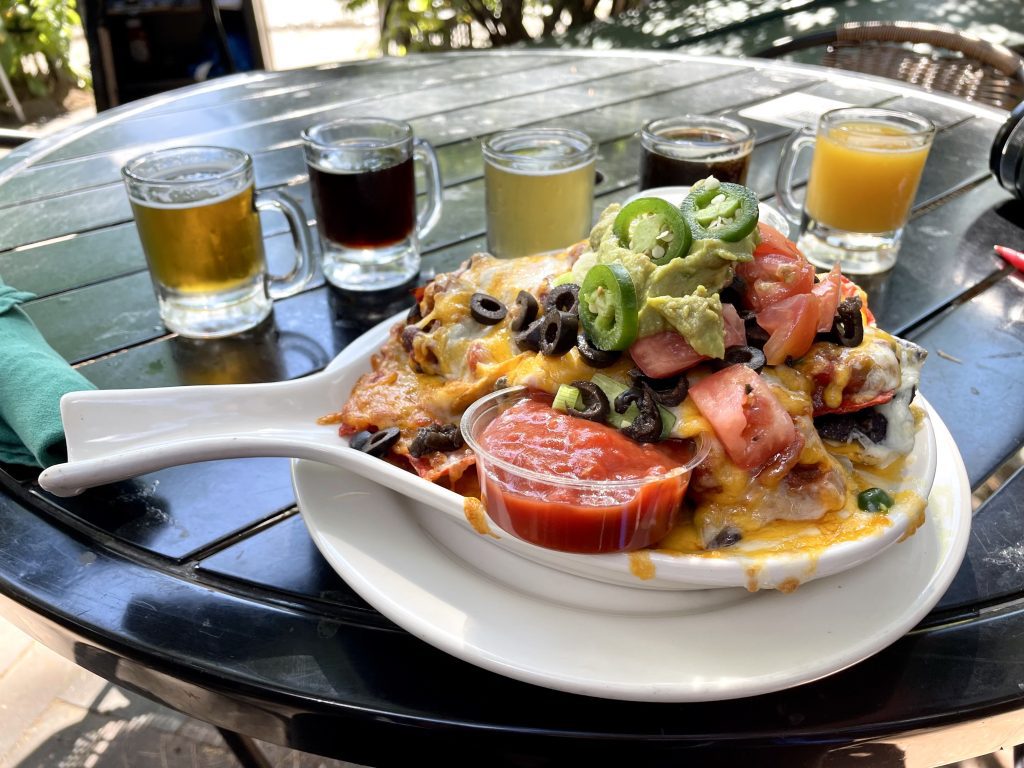 A plate of nachos in front of five tiny tasting glasses of beer.