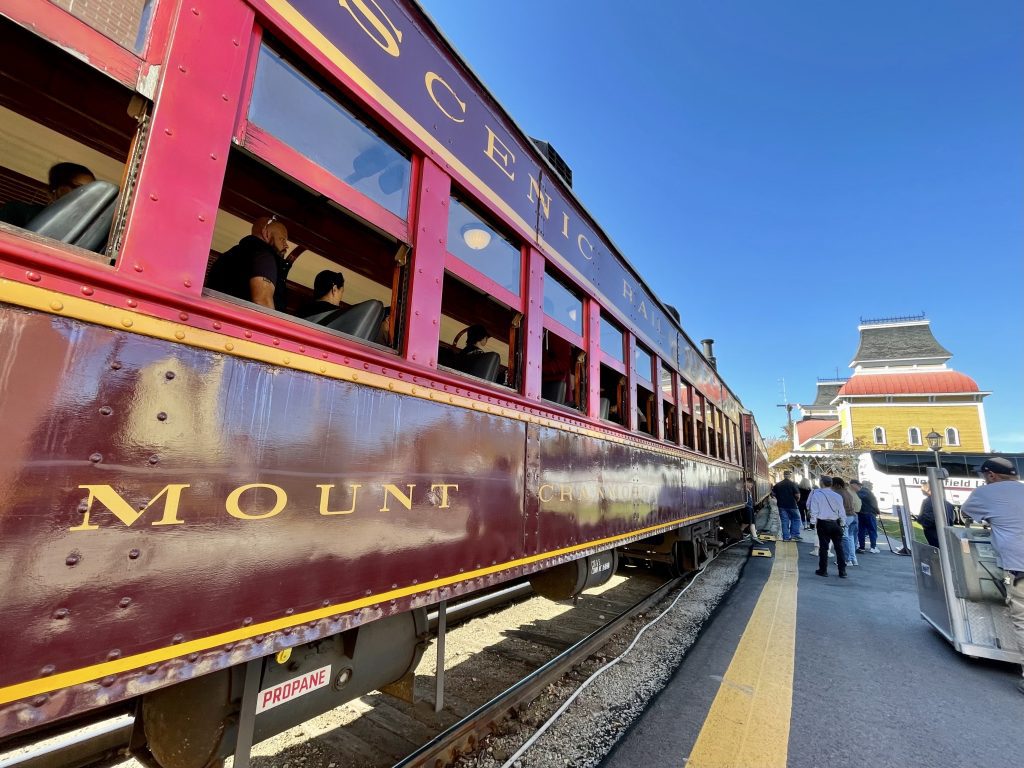 A shiny maroon train parked next to a yellow train station.