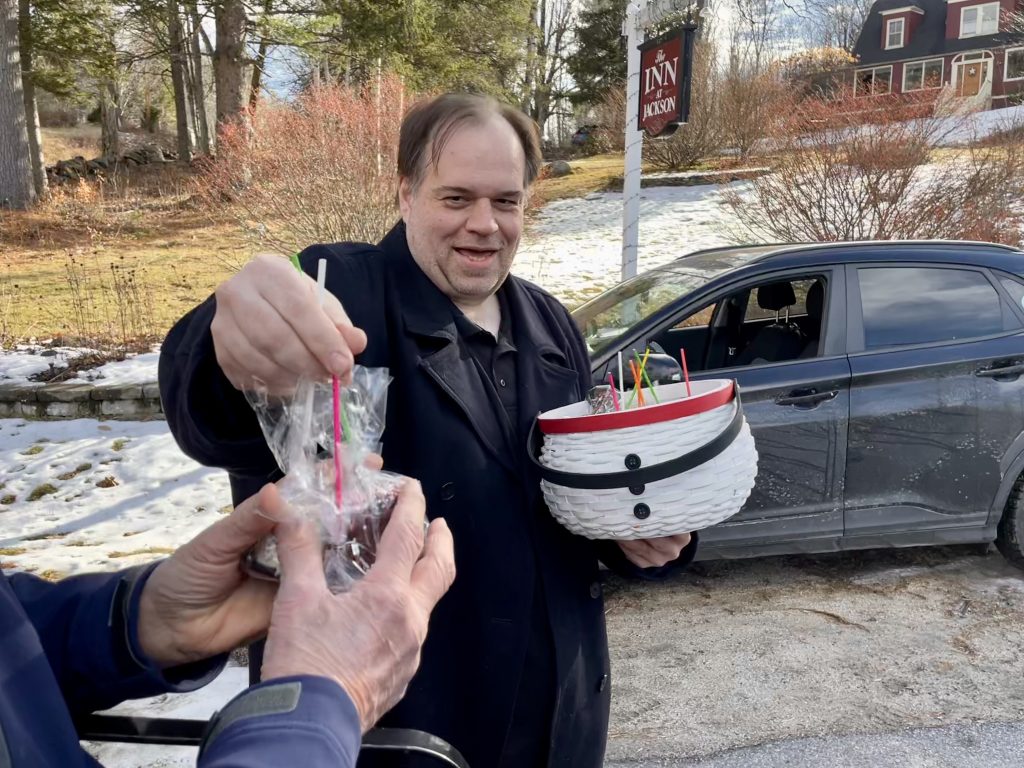 A man holding a basket and handing chocolate-covered marshmallows to an outstretched hand.