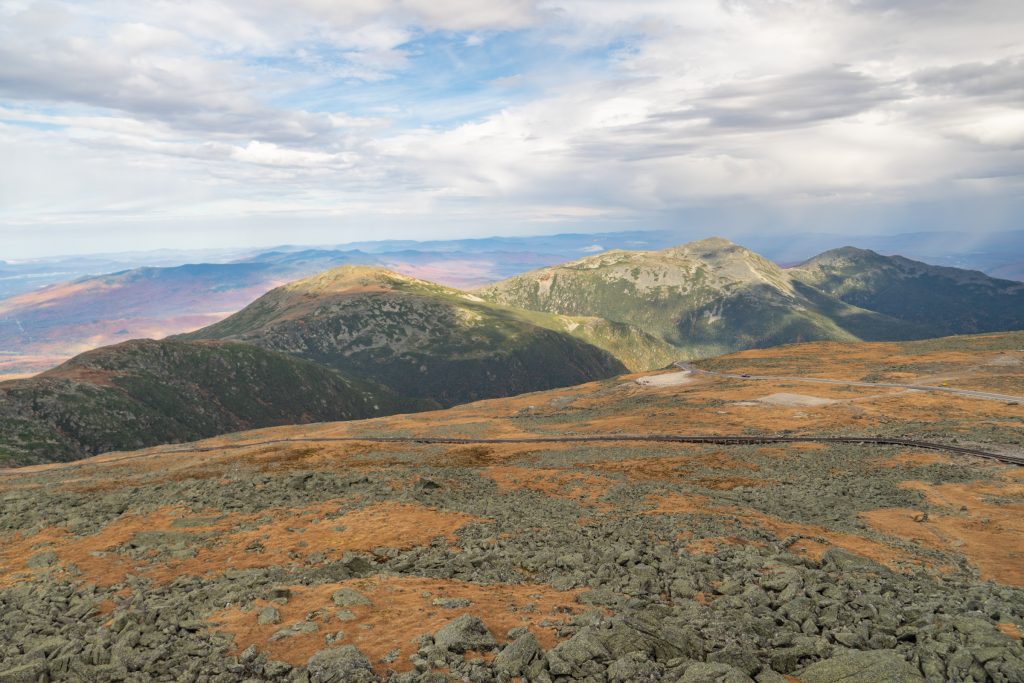 A line of round mountains covered in orange foliage underneath a cloudy sky.