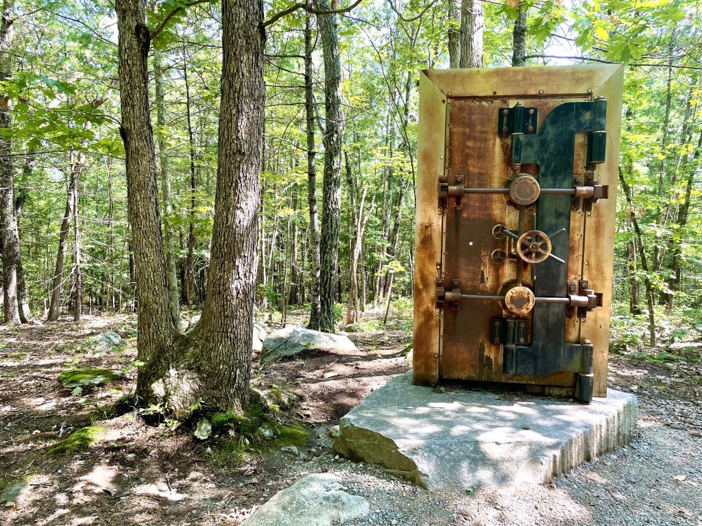 An art sculpture of a wooden door covered with knobs, in the middle of a forest.