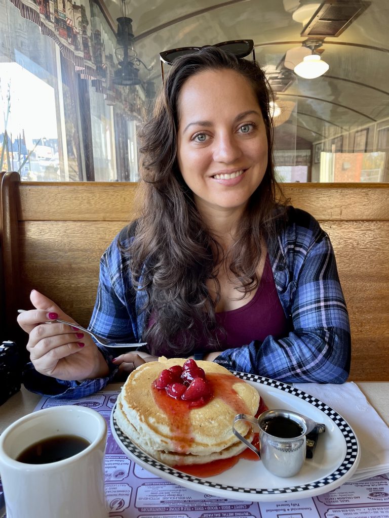 A woman in a plaid shirt smiling above a plate of pancakes topped with strawberries.