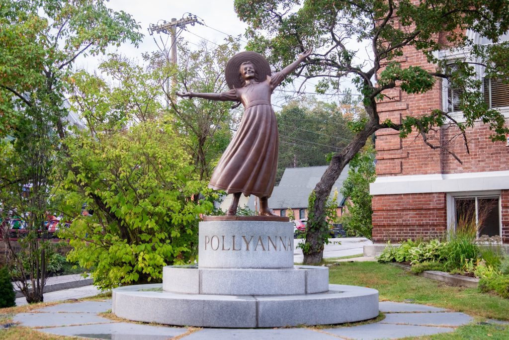 A statue of a little girl in a dress and a sun hat throwing her hands up in joy.