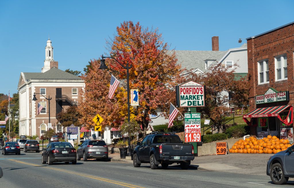 A small town downtown with church buildings, fall foliage, and stores selling pumpkins.